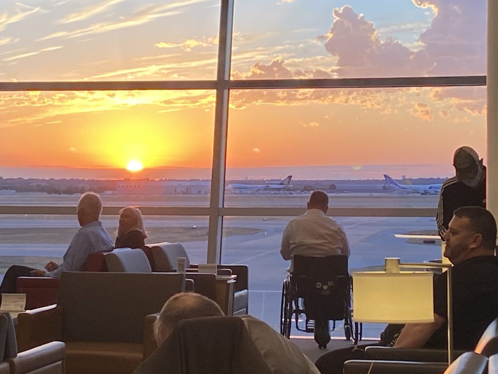 A picture of a man in a wheelchair watching a sunset from an airport window